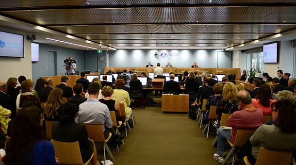 A crowded hearing room with Commissioners sitting in the distance