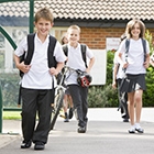 Five smiling school children walking in school yard wearing school uniform and backpacks