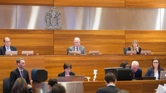 Three commissioners sitting at a bench facing a crowded hearing room. From left to right: Commissioner Andrew Murray, The Hon Justice Peter McClellan AM and Commissioner Helen Milroy