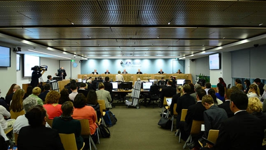 A crowded hearing room with Commissioners sitting in the distance