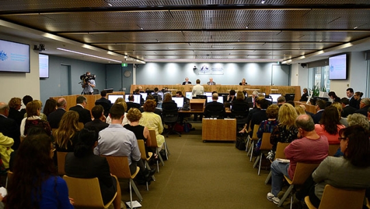 A crowded hearing room with Commissioners sitting in the distance